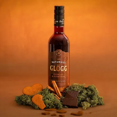 Flaska choklad och hjortronglögg från Saturnus fotograferad i en varm orange studiobelysning med mossa, kanel, choklad och pepparkakor som rekvisita.